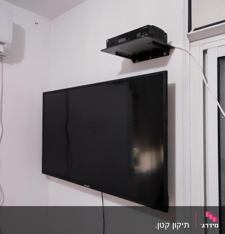 טלוויזיה תלויה על הקיר עם ממיר על מדף